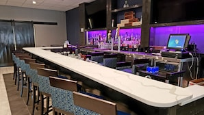 A bar area with a long counter, multiple bar stools, and shelves stocked with bottles. - Clarion Hotel Conference Center Lexington North (Lexington)