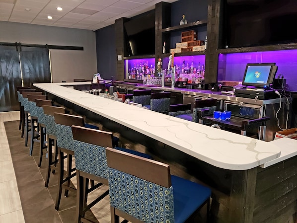 A bar area with a long counter, multiple bar stools, and shelves stocked with bottles.