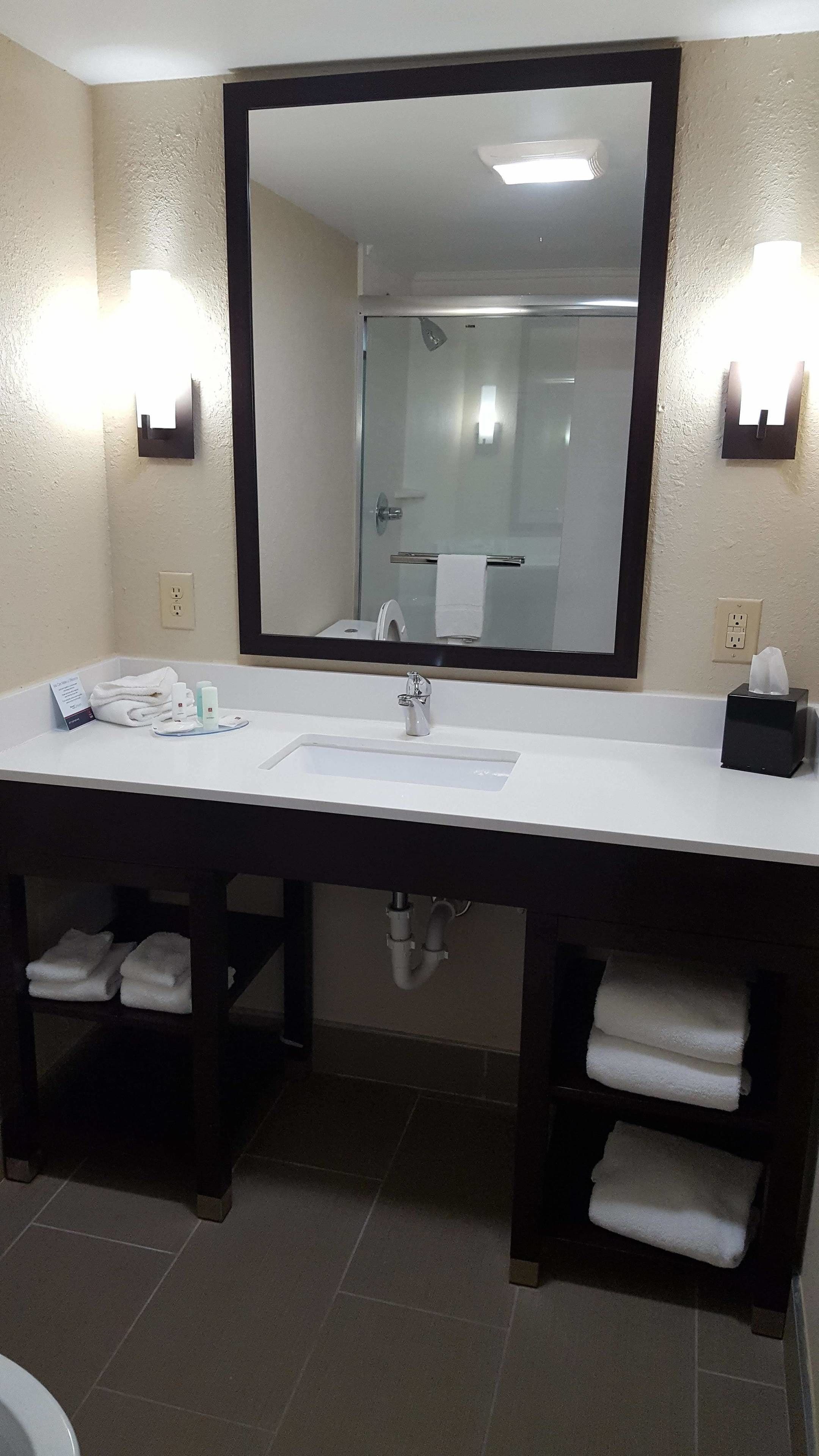 A modern bathroom with a large mirror, white sink, and two towel racks.