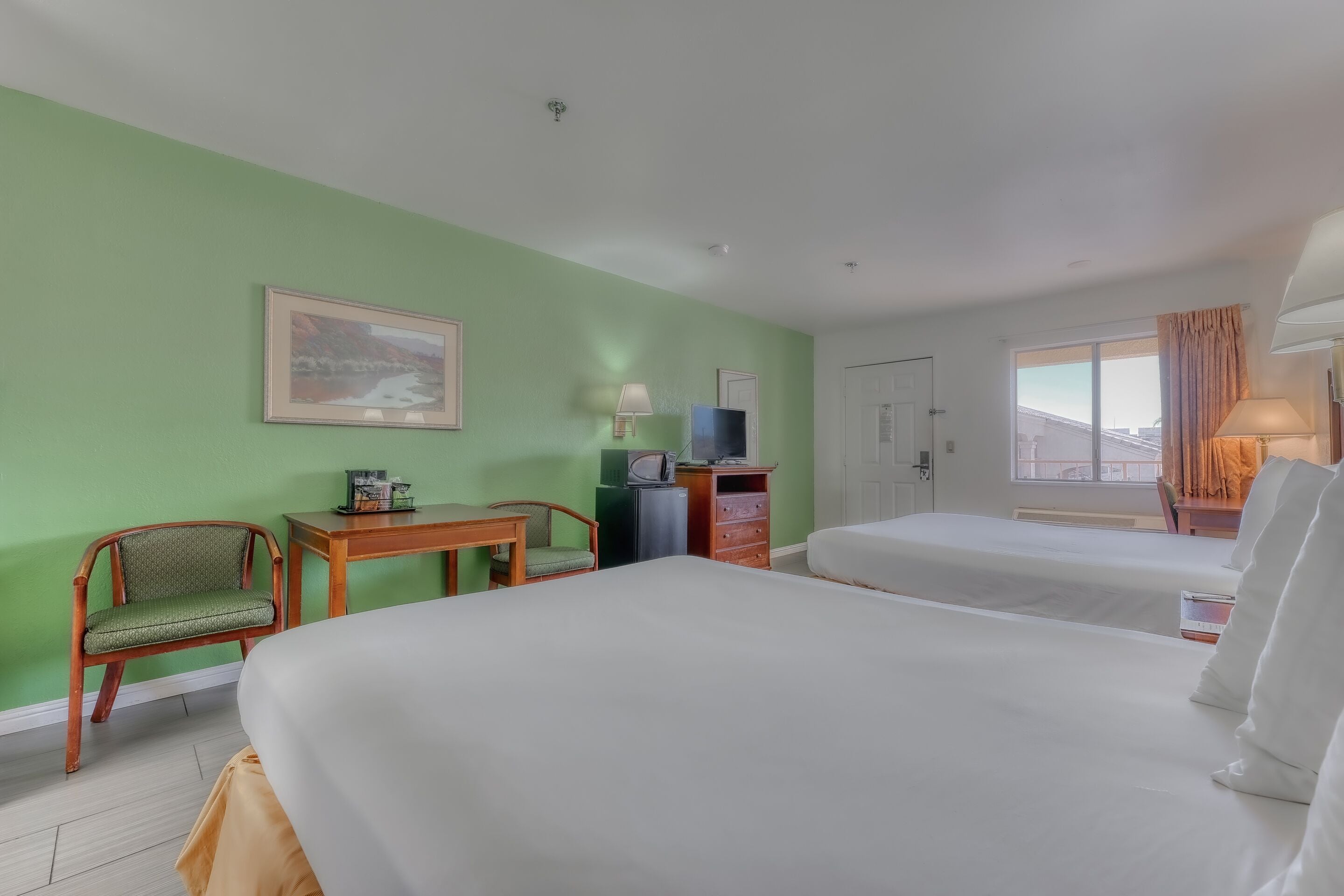 A hotel room with two beds, a desk, a chair, a TV, and a window with curtains.