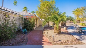 A pathway leading to a house with a tiled roof, surrounded by greenery and a pool area with outdoor seating.