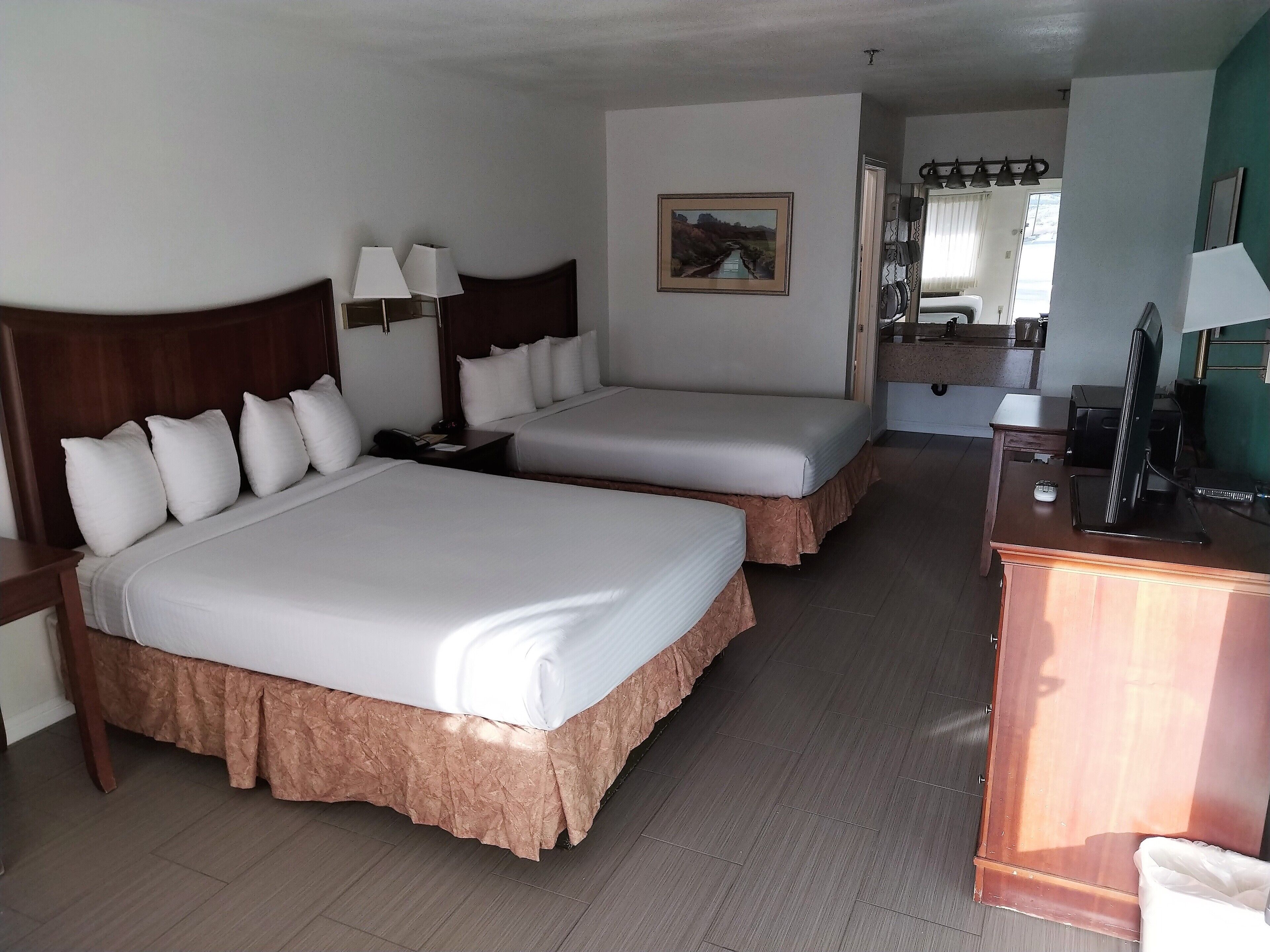 A hotel room with two beds, a desk, a telephone, and a painting on the wall.