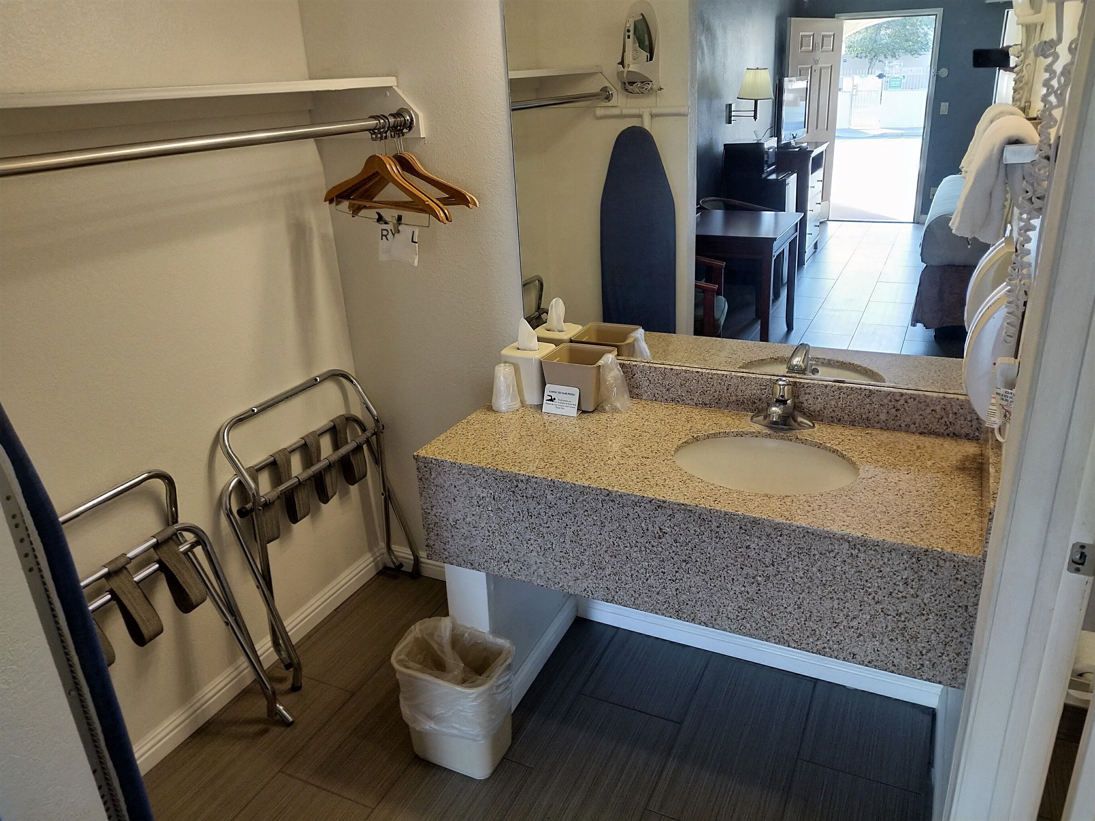 Un baño con encimera de granito, dos lavabos, un espejo, un perchero para toallas, un cesto de basura y una zona de ducha visible a través de una puerta abierta.