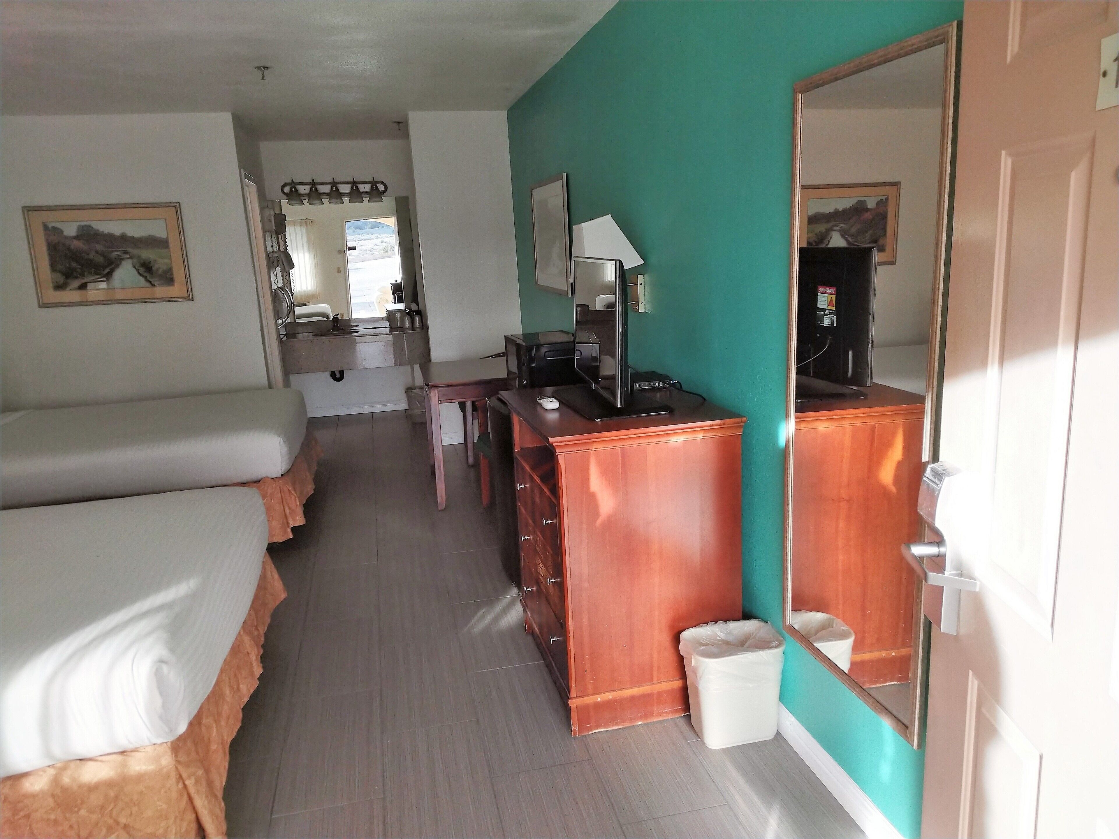 A hotel room with a bed, a desk with a computer, a mirror, and a trash bin.