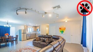 A modern living room with a leather sectional sofa, a dining area with a table and chairs, and a kitchen in the background.