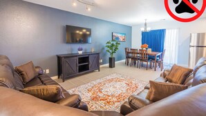 A modern living room with a sofa, a TV, a dining table, and a blue wall.