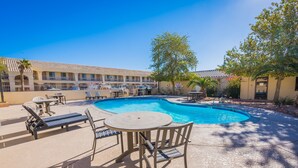 A pool area with lounge chairs, a table, and a building in the background.