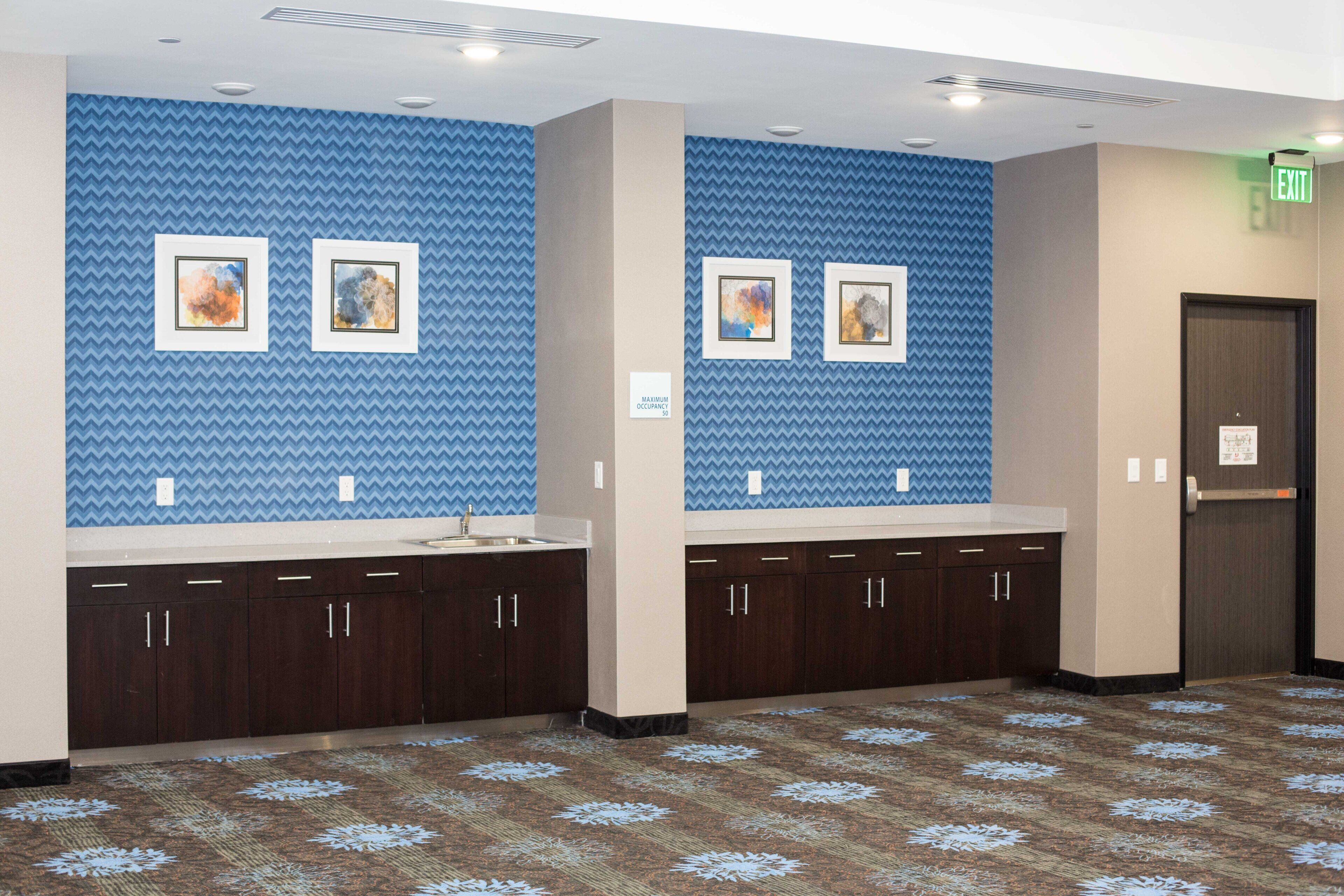A hotel restroom with blue patterned walls, two sinks, dark wooden cabinets, and a patterned carpet.