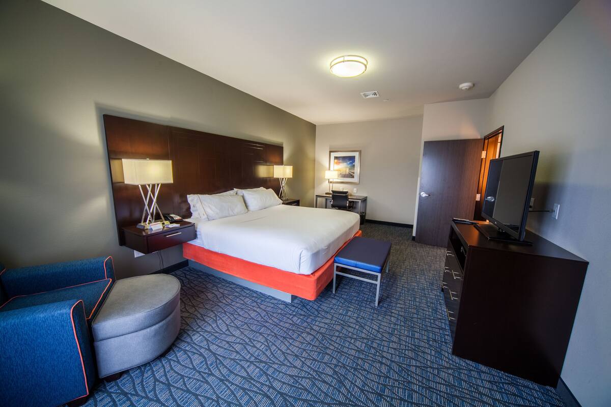 Ein Hotelzimmer mit einem großen Bett, einem Schreibtisch, einem Stuhl, einem Fernseher und einer Schreibtischlampe.