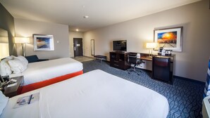 Habitación de hotel con dos camas, un escritorio con computadora, televisor y refrigerador pequeño.