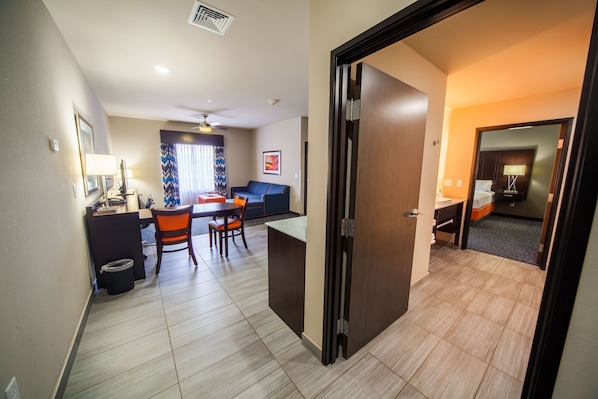 Habitación de hotel con cama, escritorio y silla. Hay una ventana con cortinas y una puerta que da a otra habitación.