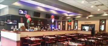 A restaurant with multiple booths and tables, a bar area, and a television screen mounted on the wall.