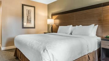 A hotel room with a large bed, a nightstand with a lamp, a framed picture on the wall, and a wooden headboard.