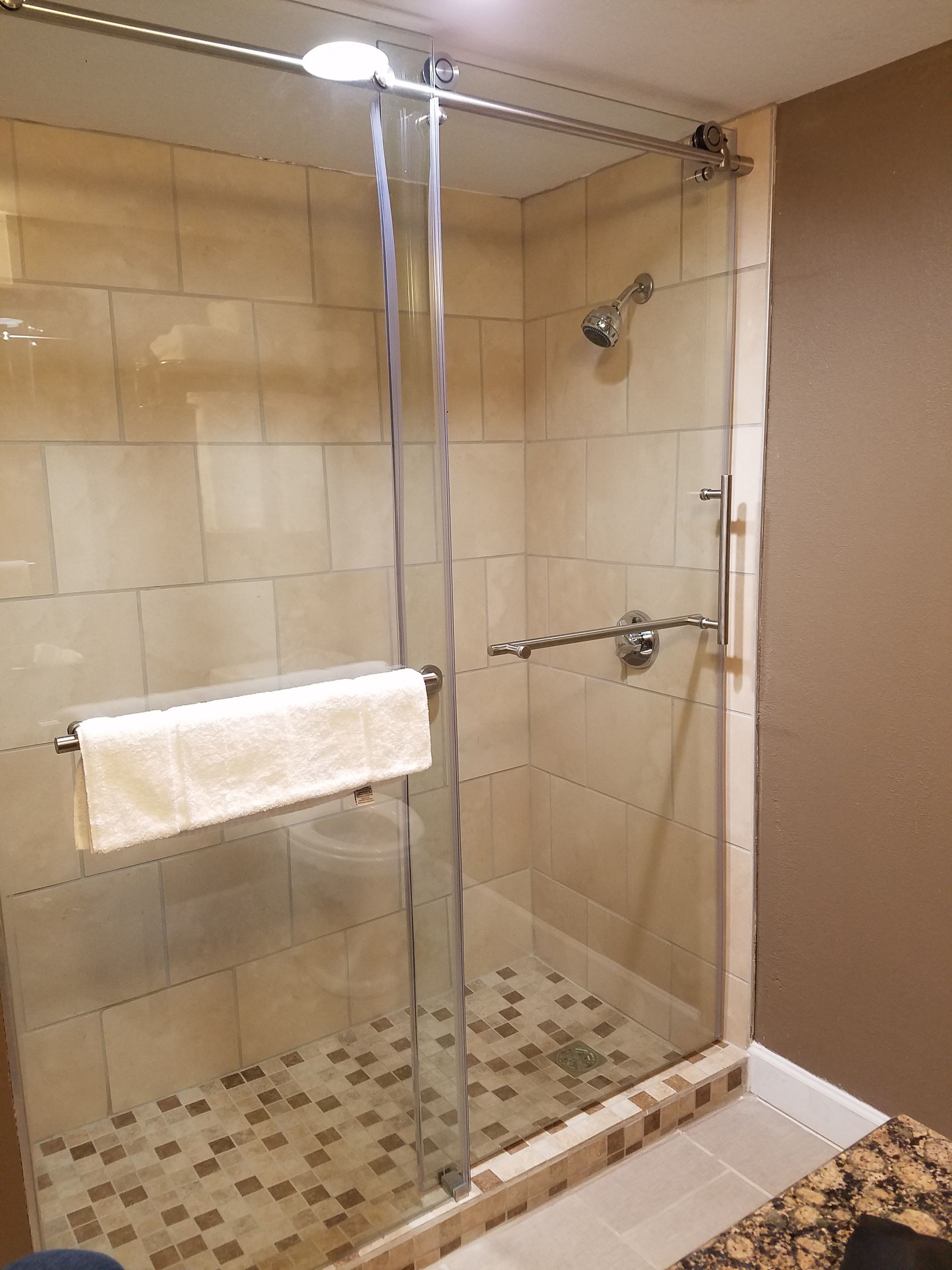 A glass-enclosed shower with a white towel hanging on a metal bar.