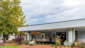 Un bâtiment moderne doté d’une entrée abritée, d’un grand arbre et d’un jardin aménagé.