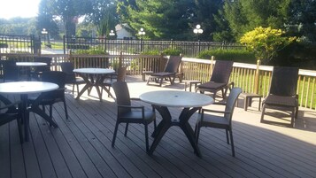 An outdoor deck with round tables and chairs, surrounded by a wooden fence and trees.