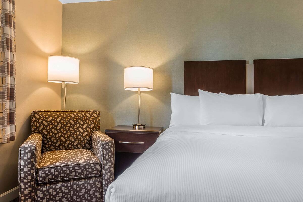 Quarto de hotel com cama, duas mesas de cabeceira, uma cadeira e duas luminárias.
