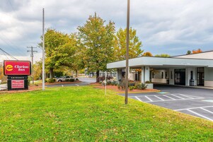A parking lot with a sign for Clarion Inn, a modern building with a covered entrance, and a tree with autumn leaves in the background.