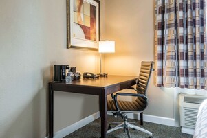 Habitación de hotel con escritorio, silla, lámpara y una obra de arte enmarcada en la pared.
