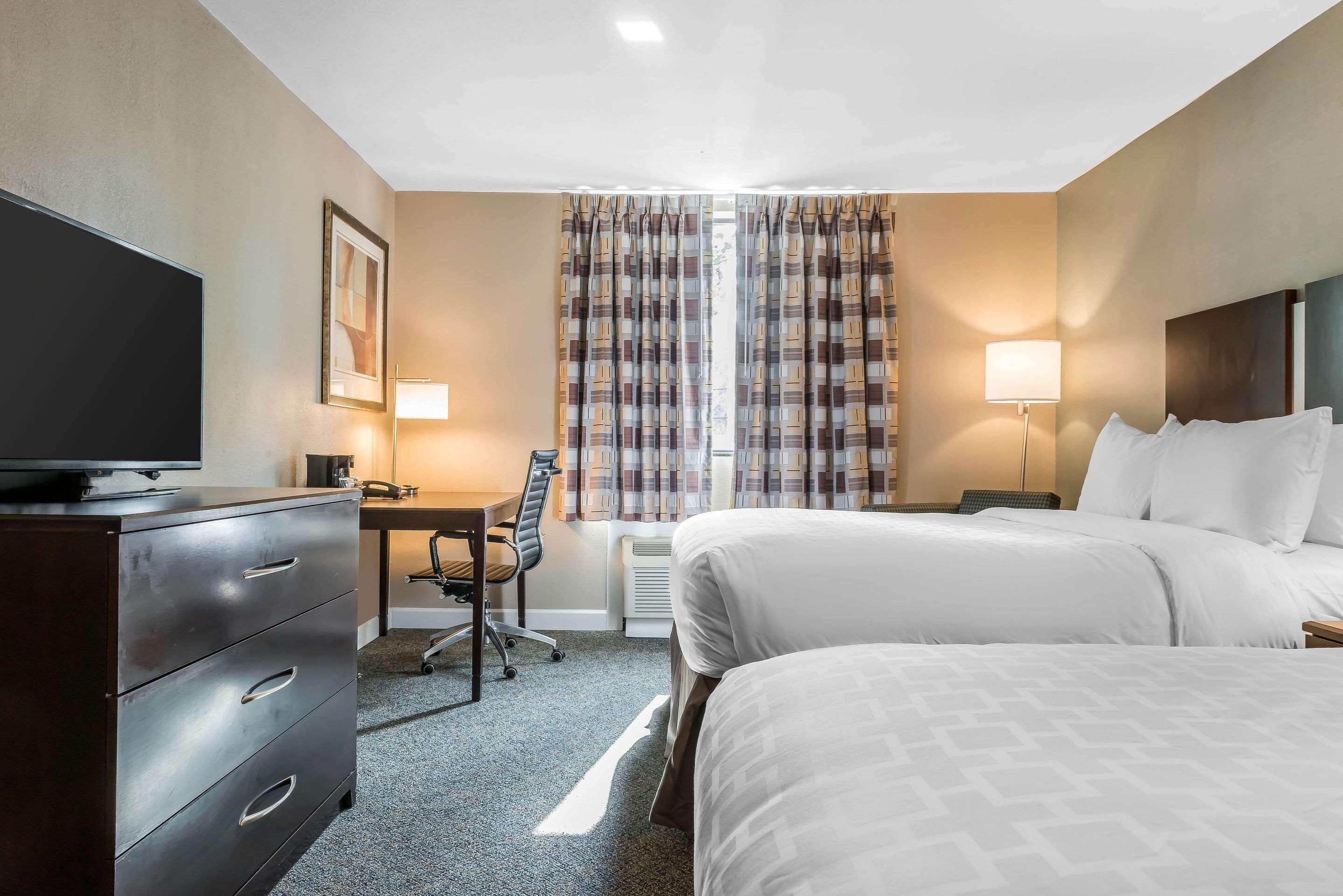 A hotel room with two beds, a desk, a chair, a television, and a lamp.