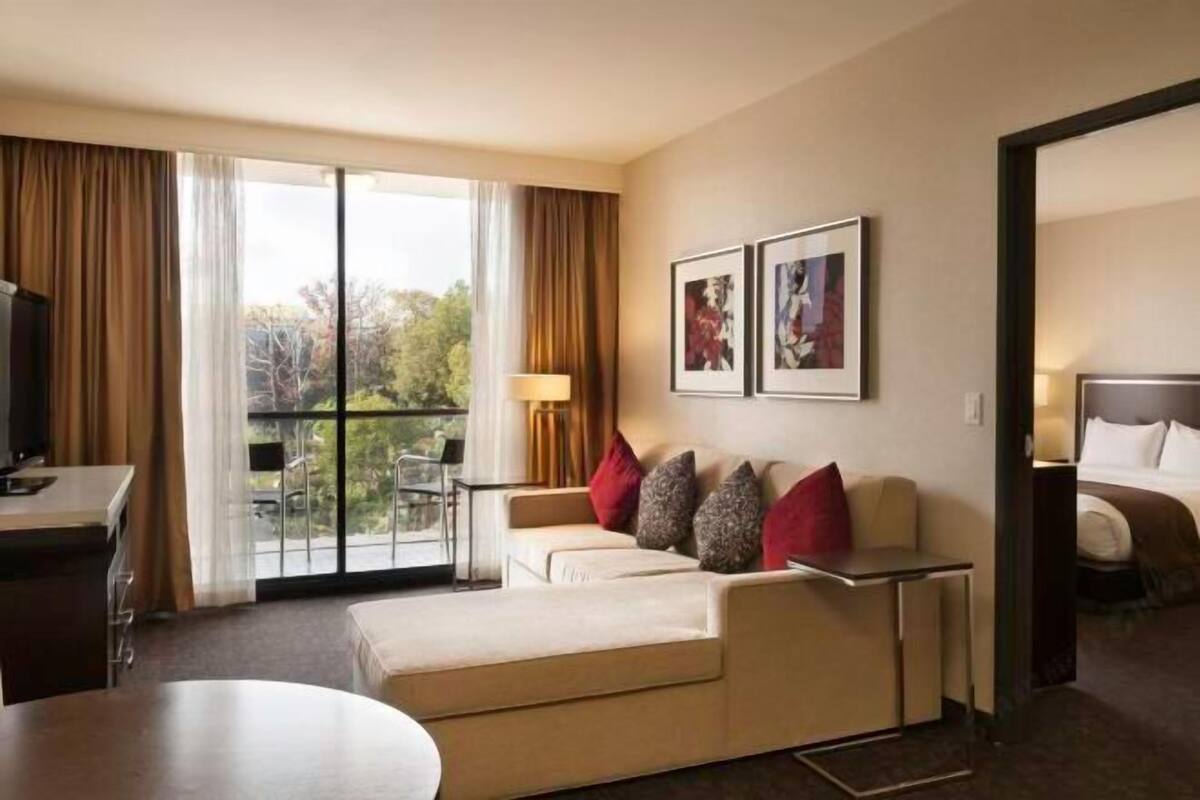 Una camera d'albergo con divano, scrivania, sedia, letto e un'ampia finestra con tende.