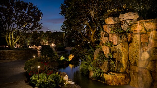 A serene garden with a water feature, stone walls, and well-lit pathways.