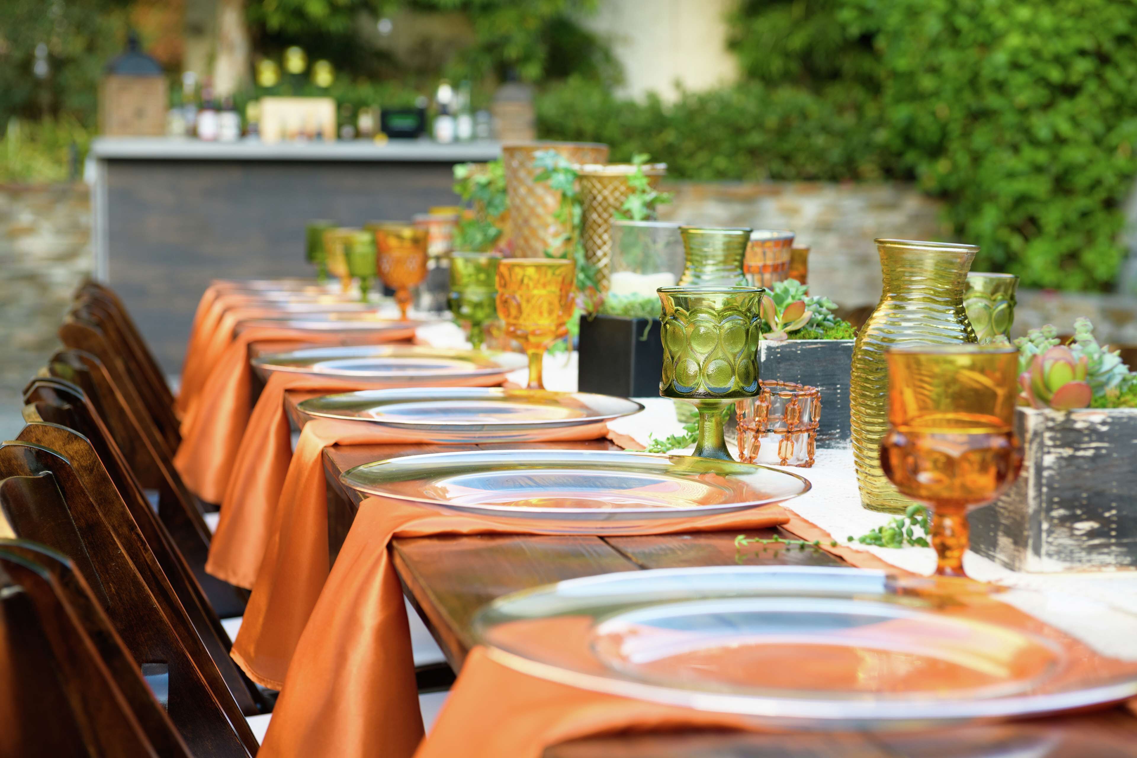 Une longue table à manger, recouverte de nappes orange, agrémentée de verres transparents et de vases décoratifs.