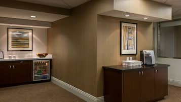 A hotel reception area with a refrigerated beverage dispenser, a coffee machine, and framed artwork on the walls.