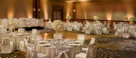 A banquet hall with round tables set for dining, each with white tablecloths and chairs, and floral centerpieces.