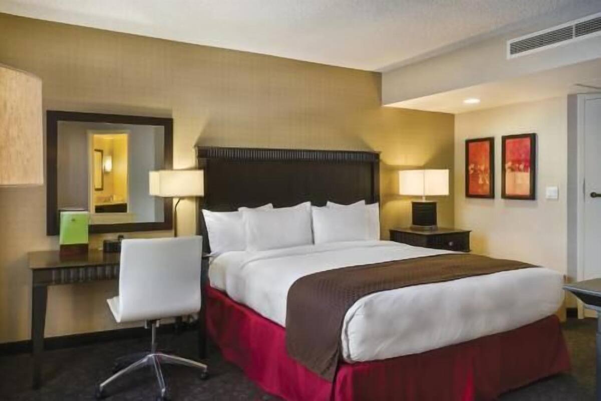 Una camera d'albergo con un letto, una scrivania, una sedia, un comodino e due lampade a parete.
