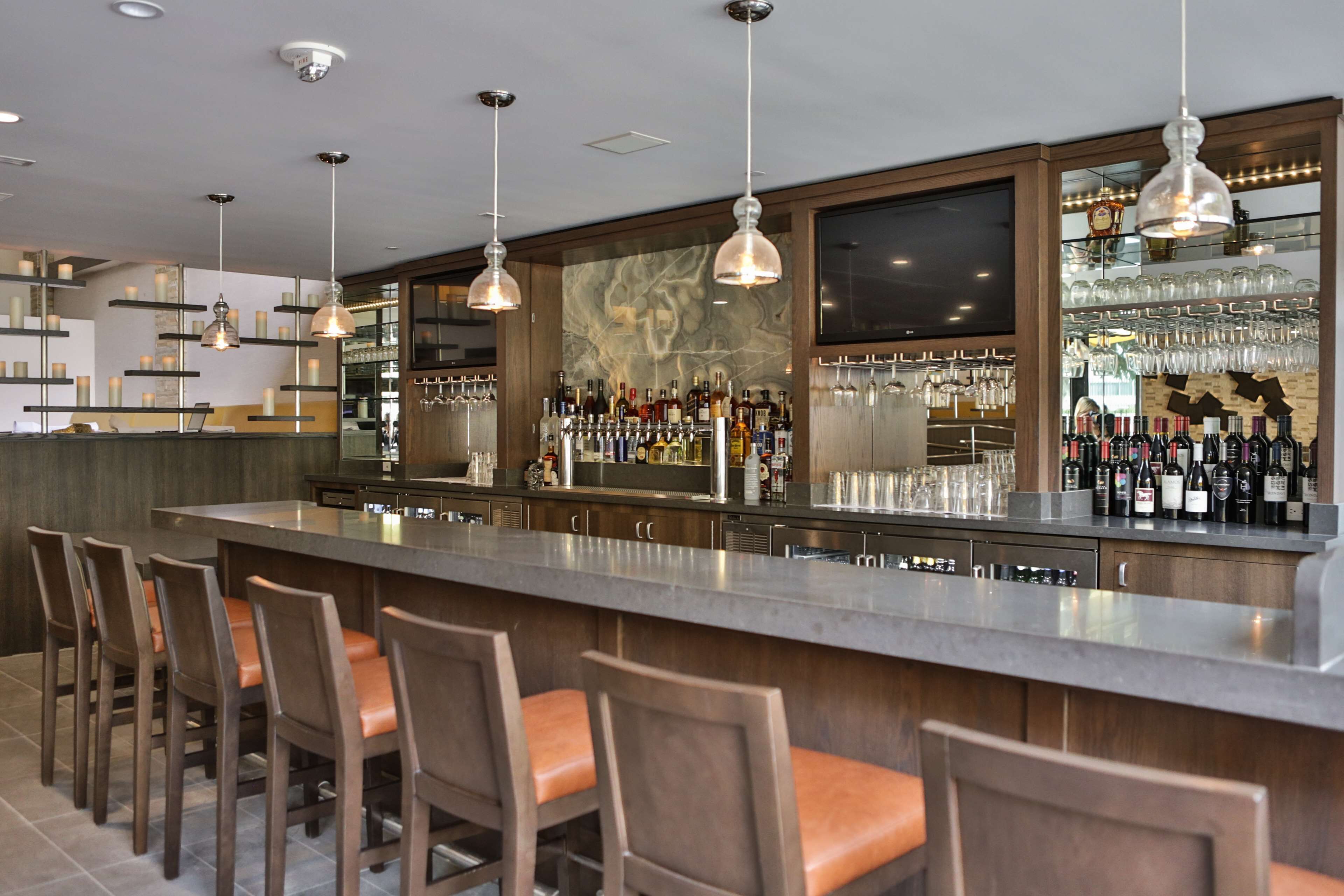 Uma área de bar com um balcão comprido, vários bancos altos e uma variedade de garrafas e copos.