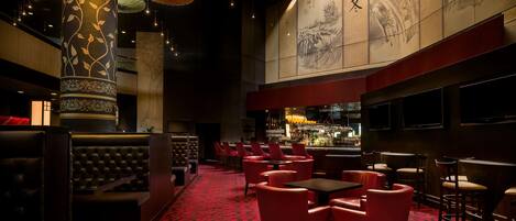 A dimly lit bar area with red upholstered seating, a patterned carpet, and traditional artwork on the walls.
