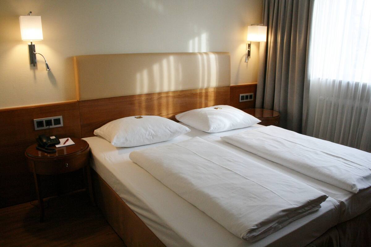 A hotel room with a large bed, two bedside tables, and wall-mounted lamps.