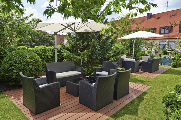 Un patio exterior con mobiliario de mimbre, dos sombrillas y una terraza de madera.