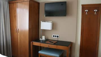Una habitación de hotel con un escritorio de madera, un televisor en la pared, un armario y una cama.