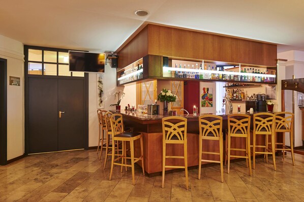 A bar area with a wooden bar counter, multiple shelves of bottles, and four wooden chairs.
