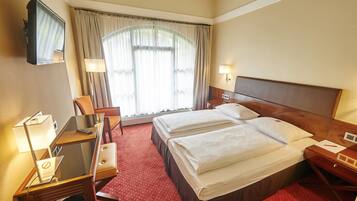 Una habitación de hotel con una cama, un escritorio con una silla, un televisor y una ventana con cortinas.