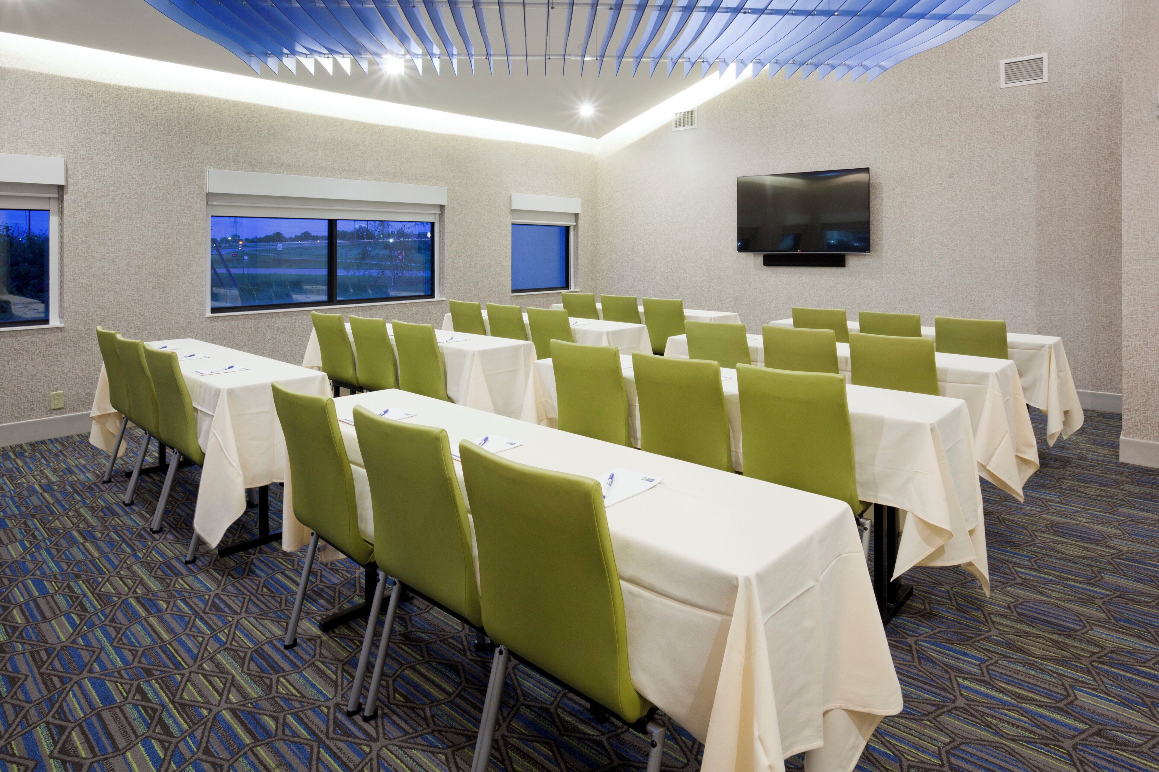 A conference room with tables and chairs, a flat-screen TV, and windows with a view.