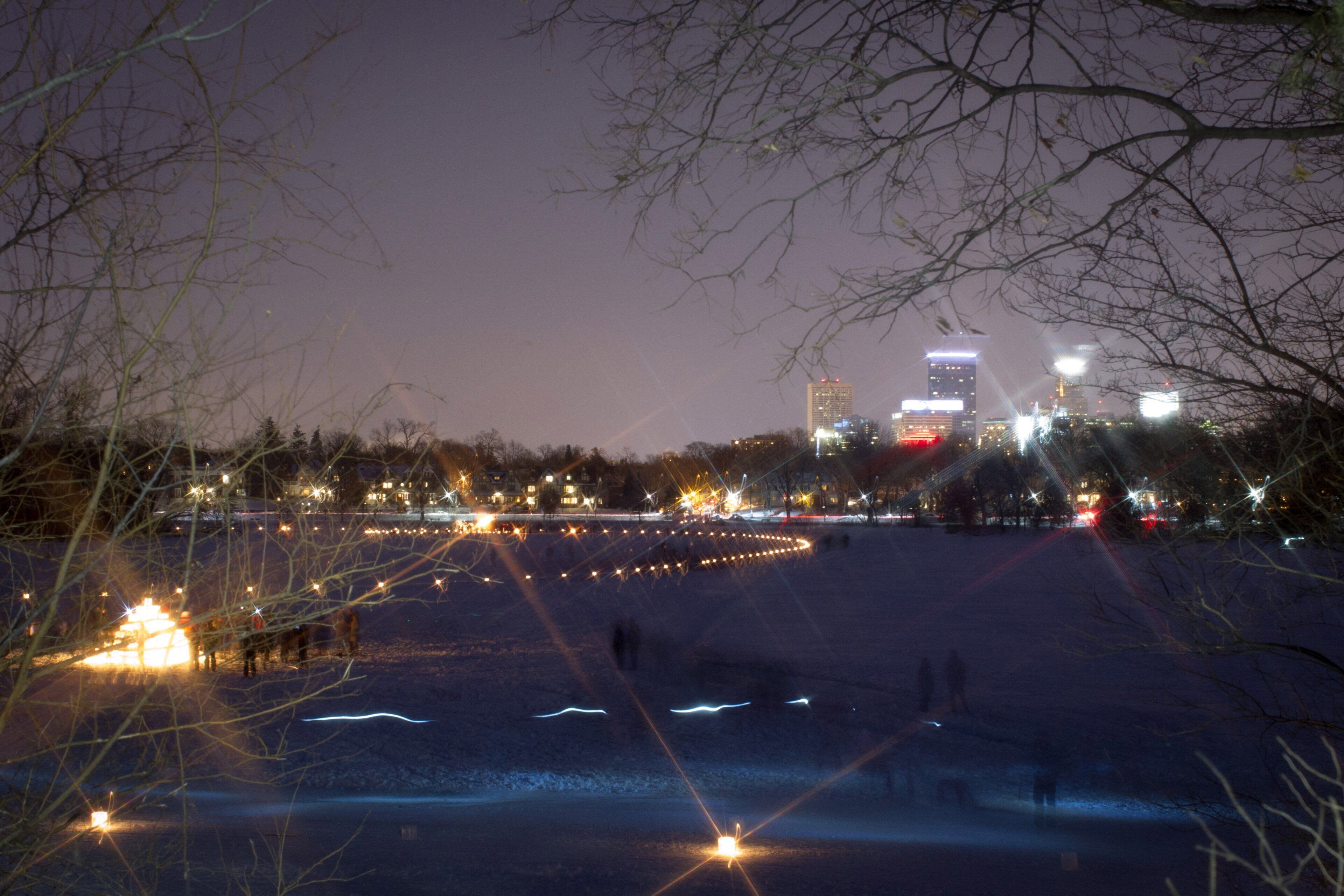 A nighttime cityscape with illuminated buildings and a snow-covered ground.