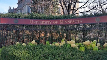 A sign for the University of Minnesota with a metal fence and greenery in front.