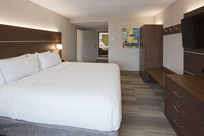 Ein Hotelzimmer mit einem großen Bett, einem Fernseher, einer Holzkommode und einer Tür zu einem Badezimmer.
