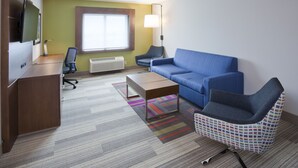 A hotel room with a wooden desk, a blue sofa, a patterned armchair, a television, and a window with a view. - Holiday Inn Express Roseville-St. Paul by IHG (Roseville)