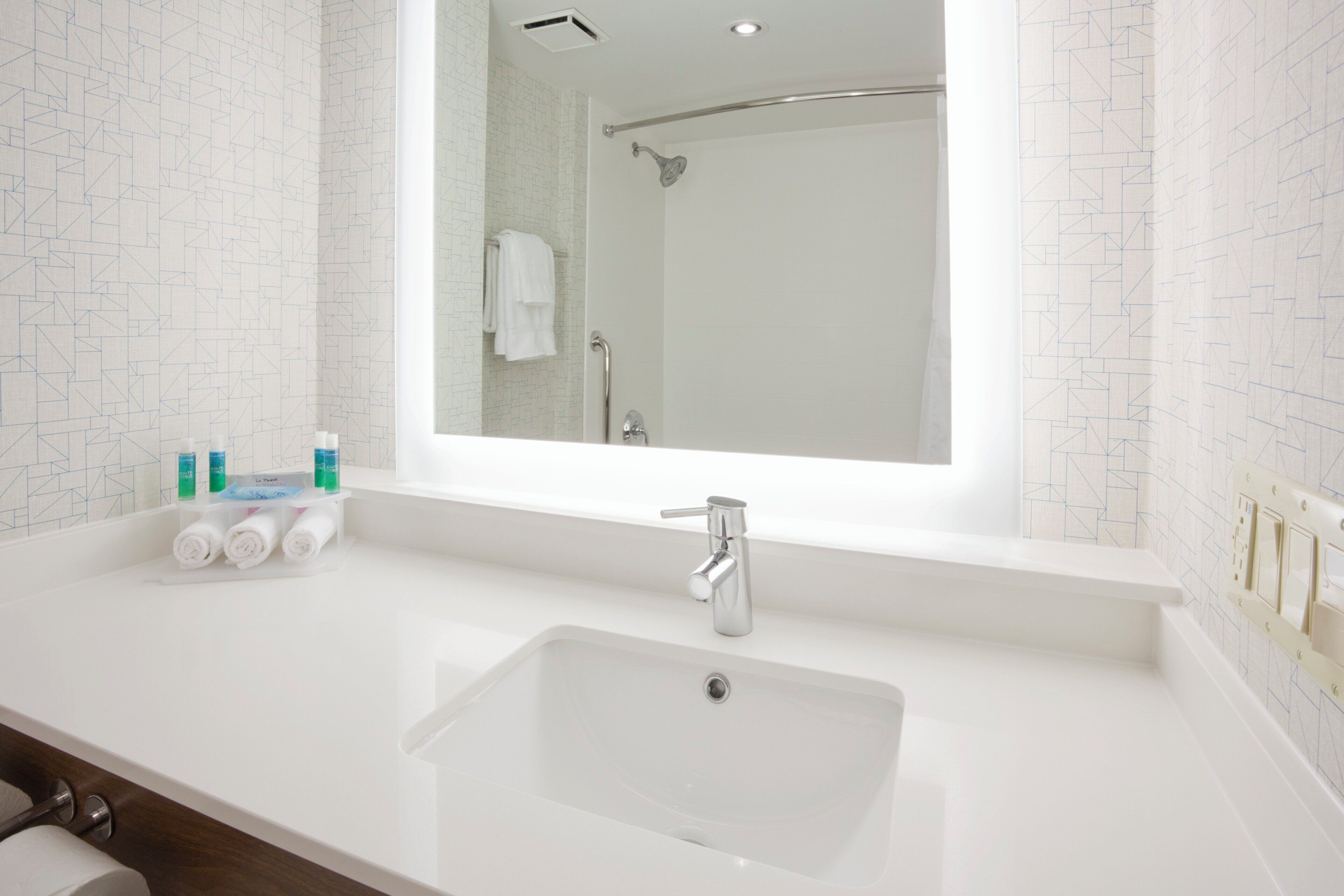A bathroom with a large mirror, a white sink, and a shower.