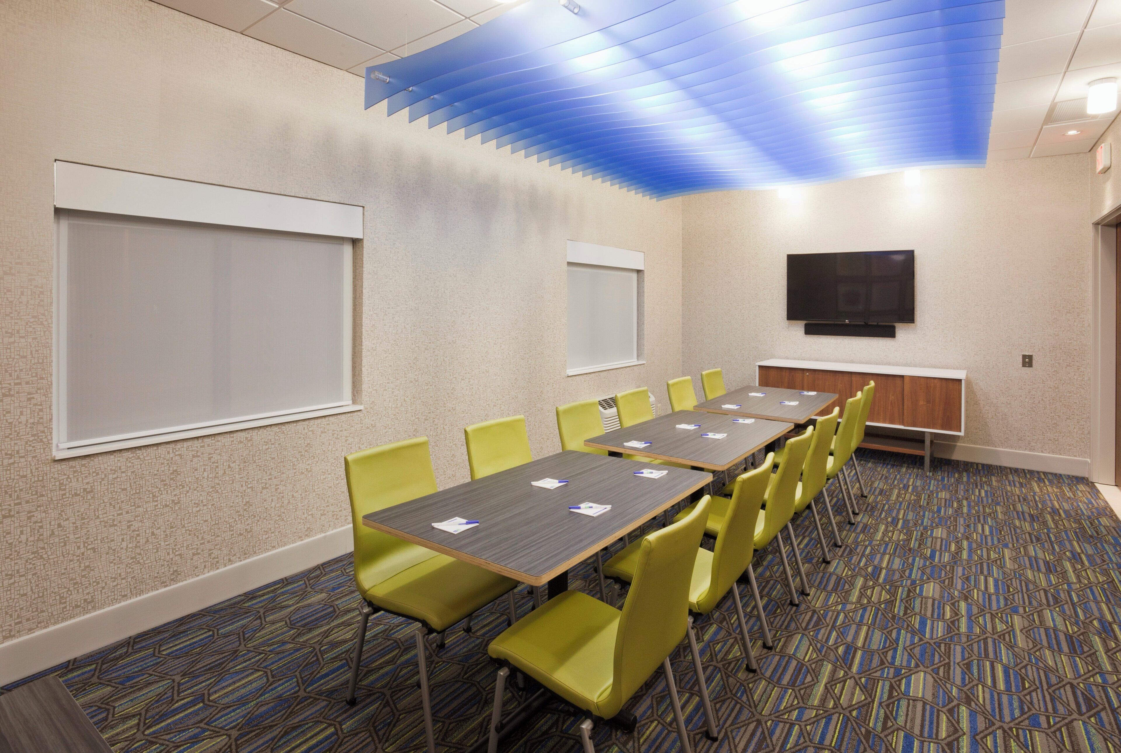 A conference room with a long table, yellow chairs, a flat-screen TV, and a patterned carpet.