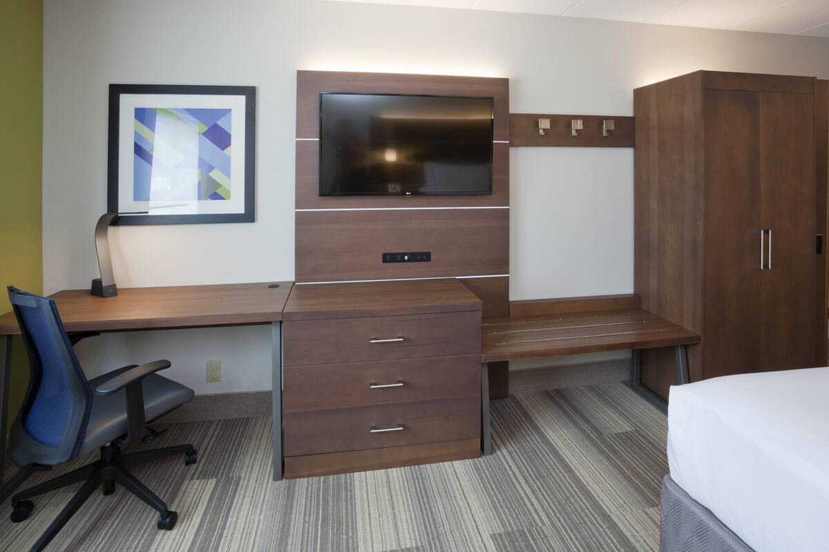 A hotel room with a wooden desk, a flat-screen TV, a bed, and a wardrobe.
