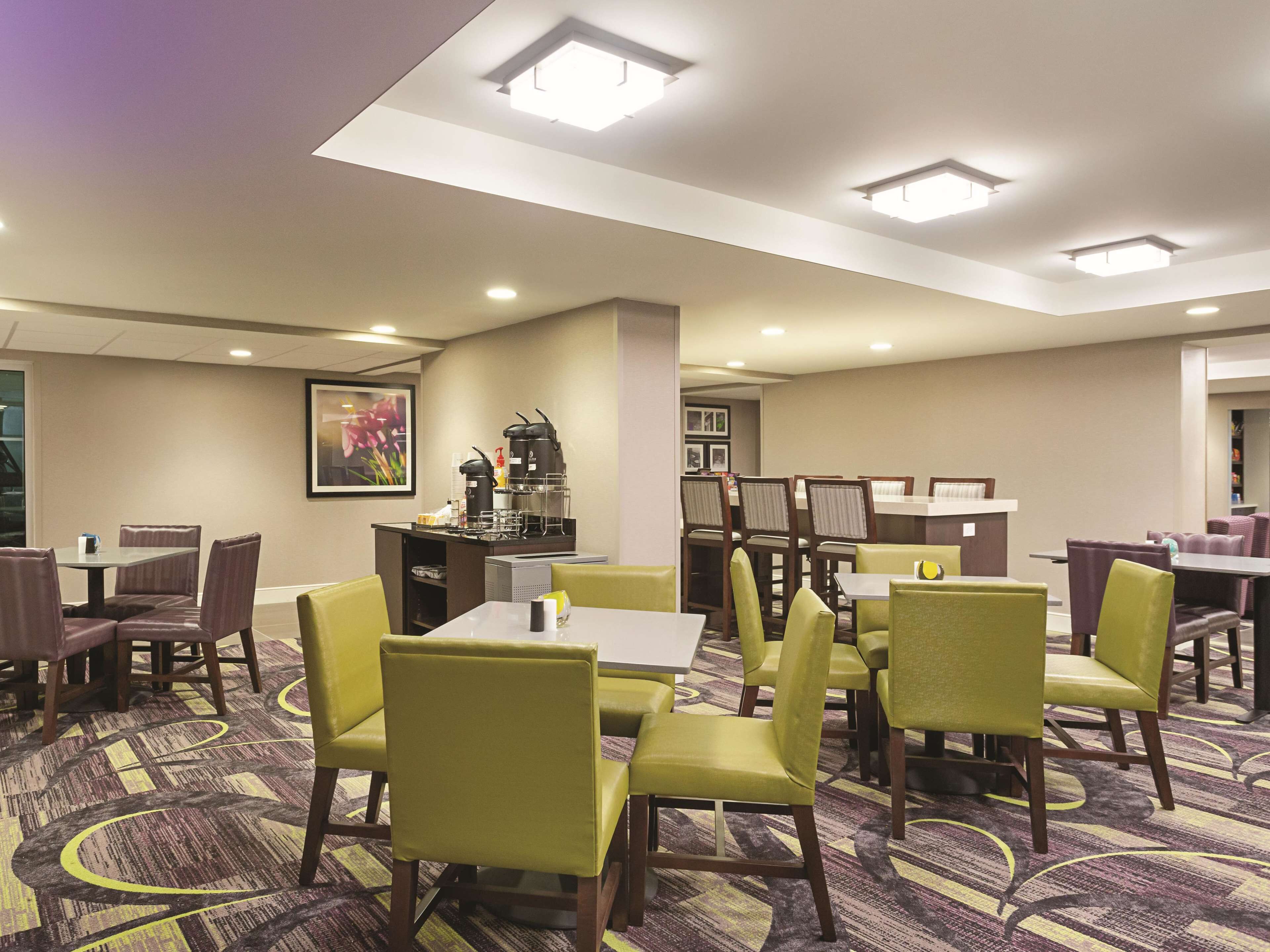 A hotel dining area with tables and chairs, a coffee station, and a framed picture on the wall.