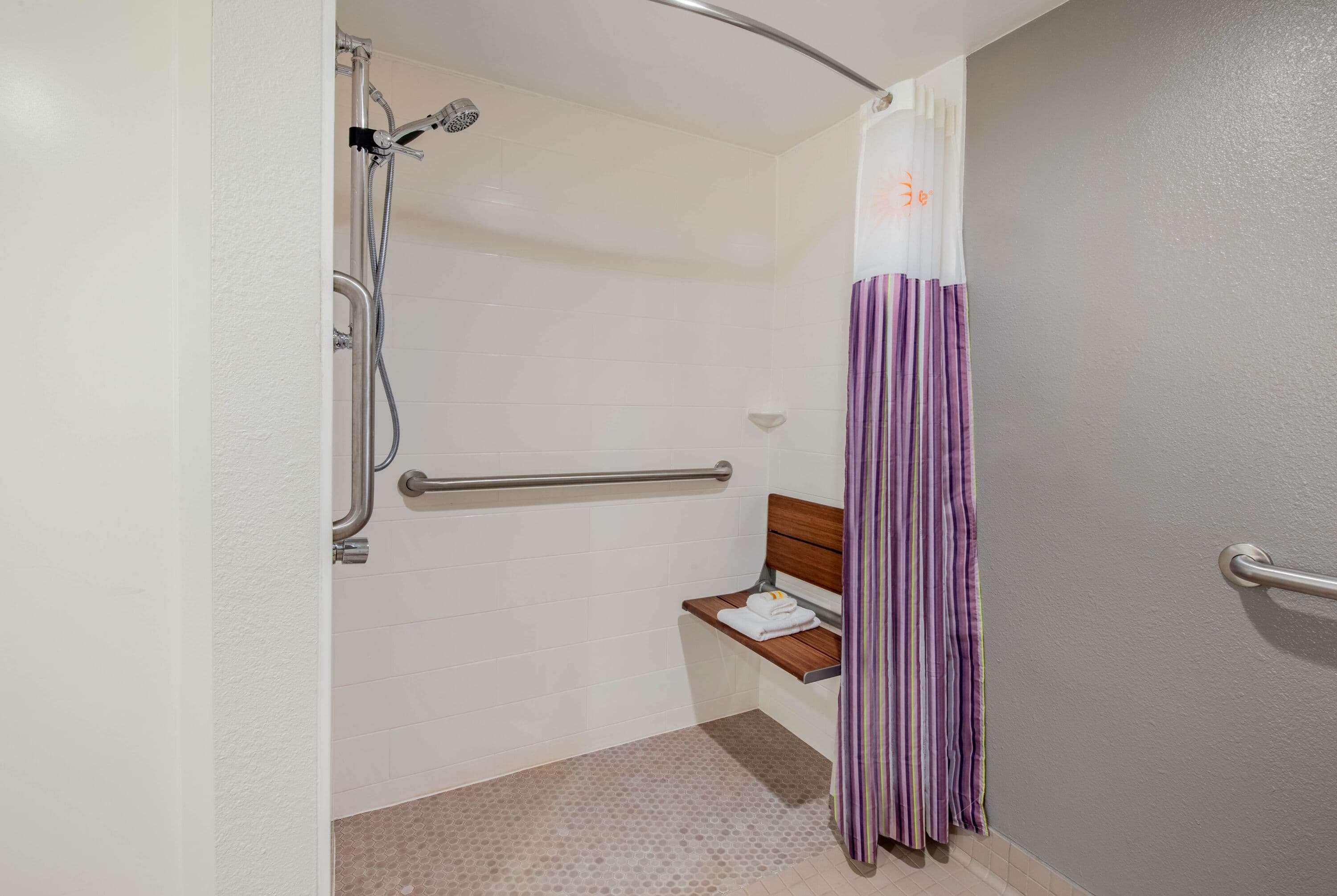 Un baño con ducha, un banco y un pasamanos.