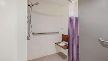 A bathroom with a shower, a bench, and a handrail.