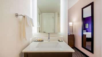A hotel bathroom with a large mirror, a white sink, and a towel rack.