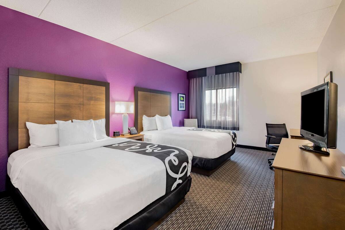 A hotel room with two beds, a desk with a TV, and a window with curtains.
